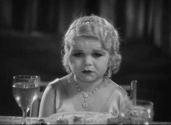 Movie still from “Freaks” (1932), directed by Tod Browning – A little girl sitting at a table in front of a glass of water; Close Up shot, High angle