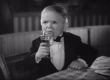 Movie still from “Freaks” (1932), directed by Tod Browning – A young boy wearing a tuxedo drinking a glass of wine; Medium shot, High angle
