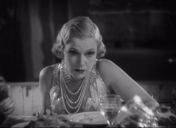 Movie still from “Freaks” (1932), directed by Tod Browning – A woman sitting at a table with a glass of wine in front of her; Close Up shot, Low angle
