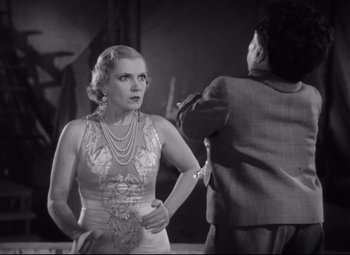 Movie still from “Freaks” (1932), directed by Tod Browning – An old photo of a woman in a dress holding a knife; Medium shot, Low angle