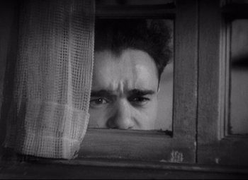 Movie still from “Freaks” (1932), directed by Tod Browning – A man looking through a window at a curtain; Close Up shot, Low angle