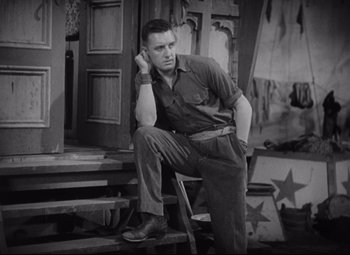 Movie still from “Freaks” (1932), directed by Tod Browning – A man sitting on a chair in front of a door; Medium shot, Low angle