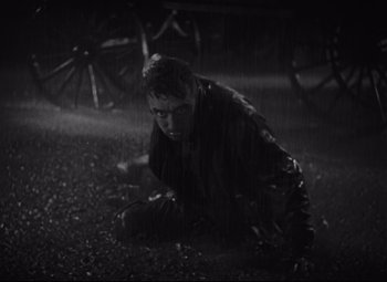 Movie still from “Freaks” (1932), directed by Tod Browning – A man crouching on the ground in the rain; Wide shot, High angle