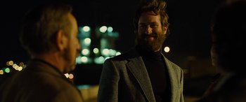 Movie still from “Free Fire” (2016), directed by Ben Wheatley – A man with a beard is smiling at the camera; Close Up shot, Over the shoulder angle