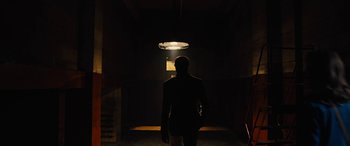 Movie still from “Free Fire” (2016), directed by Ben Wheatley – A man standing in the dark under an overhead light; Wide shot, Low angle