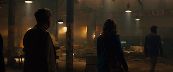 Movie still from “Free Fire” (2016), directed by Ben Wheatley – Two people are standing in a dimly - lit room; Wide shot, Over the shoulder angle