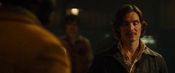 Movie still from “Free Fire” (2016), directed by Ben Wheatley – A man standing next to another man in a dark room; Close Up shot, Over the shoulder angle