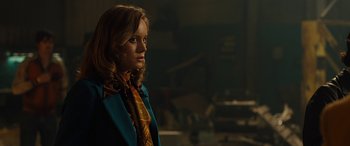 Movie still from “Free Fire” (2016), directed by Ben Wheatley – A woman in a blue coat and a yellow neck tie; Medium shot, Over the shoulder angle