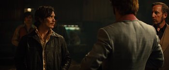 Movie still from “Free Fire” (2016), directed by Ben Wheatley – A man in a leather jacket talking to another man in a suit; Medium shot, Over the shoulder angle
