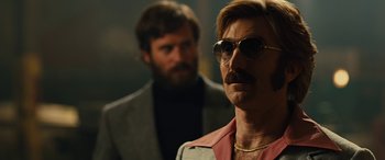 Movie still from “Free Fire” (2016), directed by Ben Wheatley – A man with a beard and mustache wearing sunglasses and a pink jacket; Close Up shot, Low angle