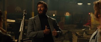 Movie still from “Free Fire” (2016), directed by Ben Wheatley – A man with a beard is holding a cell phone; Medium shot, Low angle