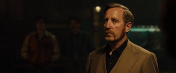 Movie still from “Free Fire” (2016), directed by Ben Wheatley – A man in a brown jacket and a black shirt; Close Up shot, Over the shoulder angle