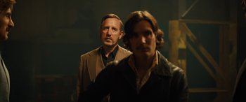 Movie still from “Free Fire” (2016), directed by Ben Wheatley – A man and a woman standing next to each other; Medium shot, Over the shoulder angle