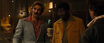 Movie still from “Free Fire” (2016), directed by Ben Wheatley – Two men standing next to each other in front of a building; Medium shot, Low angle