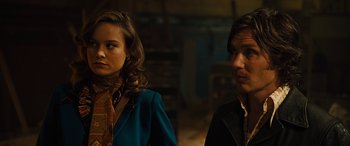 Movie still from “Free Fire” (2016), directed by Ben Wheatley – A man and a woman standing next to each other; Close Up shot, Over the shoulder angle
