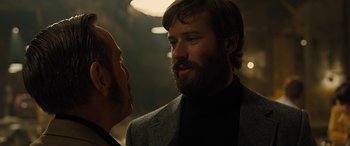 Movie still from “Free Fire” (2016), directed by Ben Wheatley – A man with a beard talking to another man in a dark room; Close Up shot, Over the shoulder angle