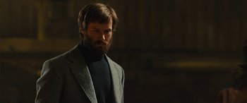 Movie still from “Free Fire” (2016), directed by Ben Wheatley – A man with a beard wearing a suit and tie; Medium shot, Low angle