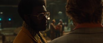 Movie still from “Free Fire” (2016), directed by Ben Wheatley – A person wearing glasses with other people in the background; Close Up shot, Over the shoulder angle