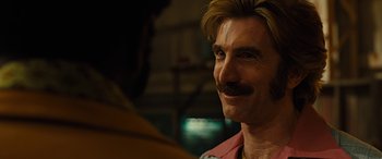 Movie still from “Free Fire” (2016), directed by Ben Wheatley – A person with a mustache smiling; Close Up shot, Over the shoulder angle