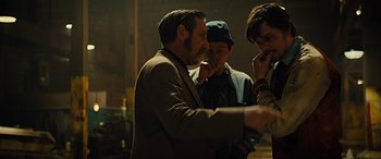 Movie still from “Free Fire” (2016), directed by Ben Wheatley – A group of people standing around in a dark room; Medium shot, Over the shoulder angle