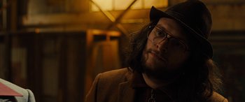 Movie still from “Free Fire” (2016), directed by Ben Wheatley – A man with long hair wearing glasses and a hat; Close Up shot, Low angle