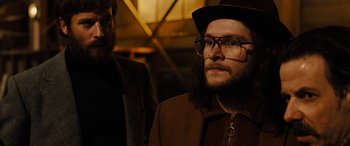 Movie still from “Free Fire” (2016), directed by Ben Wheatley – A man with a beard wearing glasses and a hat; Close Up shot, Over the shoulder angle