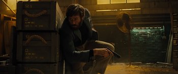 Movie still from “Free Fire” (2016), directed by Ben Wheatley – A man sitting on the ground holding a gun; Medium shot, Low angle