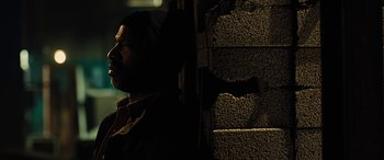 Movie still from “Free Fire” (2016), directed by Ben Wheatley – A man standing next to a wall in the dark; Close Up shot, Low angle