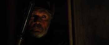 Movie still from “Free Fire” (2016), directed by Ben Wheatley – An old man with a beard and a hat is looking out of a window; Close Up shot, Low angle