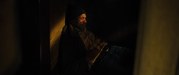 Movie still from “Free Fire” (2016), directed by Ben Wheatley – A man sitting on the ground in the dark; Medium shot, High angle