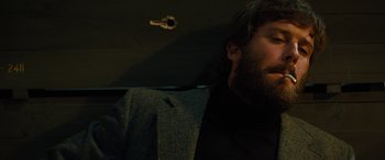 Movie still from “Free Fire” (2016), directed by Ben Wheatley – A man with a beard is sitting in a dark room; Close Up shot, Low angle