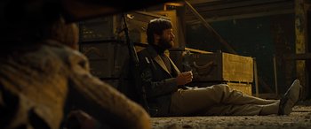 Movie still from “Free Fire” (2016), directed by Ben Wheatley – A man sitting on the ground holding a gun; Medium shot, Low angle