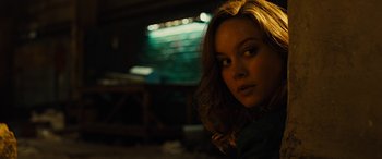 Movie still from “Free Fire” (2016), directed by Ben Wheatley – A beautiful young woman with long brown hair and green eyes; Close Up shot, Over the shoulder angle