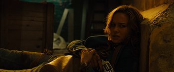 Movie still from “Free Fire” (2016), directed by Ben Wheatley – A woman holding a gun while sitting on a chair; Close Up shot, Over the shoulder angle
