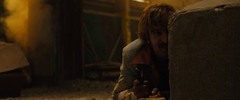Movie still from “Free Fire” (2016), directed by Ben Wheatley – A man sitting on the ground with a pen in his mouth; Close Up shot, Over the shoulder angle