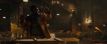 Movie still from “Free Fire” (2016), directed by Ben Wheatley – A man standing on top of a truck in an industrial setting; Medium shot, Low angle
