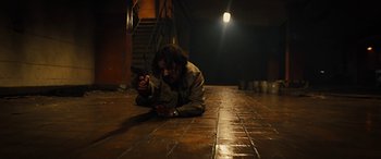 Movie still from “Free Fire” (2016), directed by Ben Wheatley – A person laying on the ground holding a gun; Wide shot, High angle