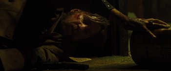 Movie still from “Free Fire” (2016), directed by Ben Wheatley – A man is laying down on the ground with a knife in his hand; Close Up shot, Low angle