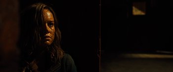 Movie still from “Free Fire” (2016), directed by Ben Wheatley – A woman is standing in the dark looking at the camera; Close Up shot, Over the shoulder angle