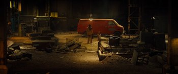 Movie still from “Free Fire” (2016), directed by Ben Wheatley – A man standing next to a red van in a garage; Wide shot, Low angle