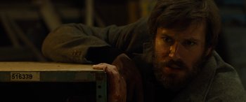 Movie still from “Free Fire” (2016), directed by Ben Wheatley – A man with a beard leaning on a box; Close Up shot, Low angle