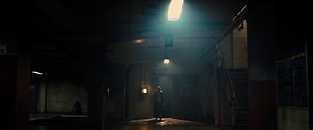 Movie still from “Free Fire” (2016), directed by Ben Wheatley – A person standing in a dark room with a light shining on them; Extreme Wide shot, Low angle