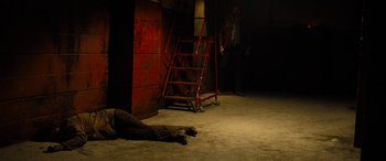 Movie still from “Free Fire” (2016), directed by Ben Wheatley – A man laying on the ground next to a ladder; Wide shot, High angle