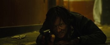 Movie still from “Free Fire” (2016), directed by Ben Wheatley – A man is holding a gun and looking at the camera; Close Up shot, High angle