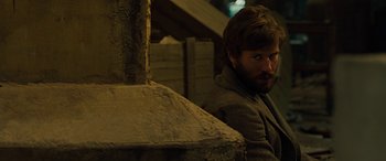 Movie still from “Free Fire” (2016), directed by Ben Wheatley – A man with a goatee sitting in front of an oven; Medium shot, Over the shoulder angle