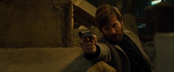 Movie still from “Free Fire” (2016), directed by Ben Wheatley – A man holding a gun in his hand; Close Up shot, Over the shoulder angle