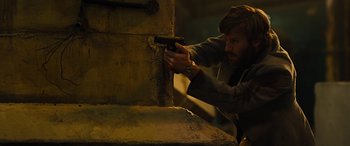 Movie still from “Free Fire” (2016), directed by Ben Wheatley – A man holding a gun in his hand; Medium shot, Low angle
