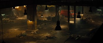 Movie still from “Free Fire” (2016), directed by Ben Wheatley – A man laying on the ground in a dark room; Extreme Wide shot, High angle