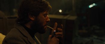 Movie still from “Free Fire” (2016), directed by Ben Wheatley – A man smoking a cigarette while looking at his cell phone; Close Up shot, Low angle
