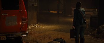Movie still from “Free Fire” (2016), directed by Ben Wheatley – A man is lying on the ground next to a dead body; Wide shot, High angle
